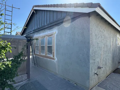 Windows masked off and fresh stucco coating applied during an exterior repaint