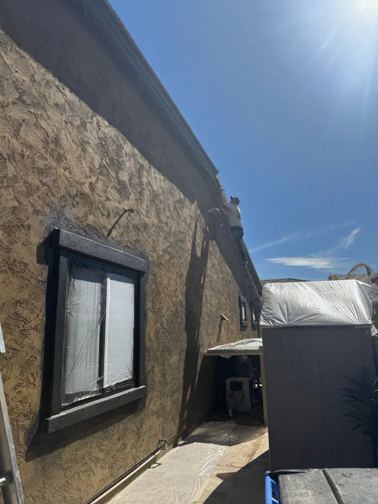 Painter cutting in freshly painted fascia from a ladder on a two-story Mesa stucco home