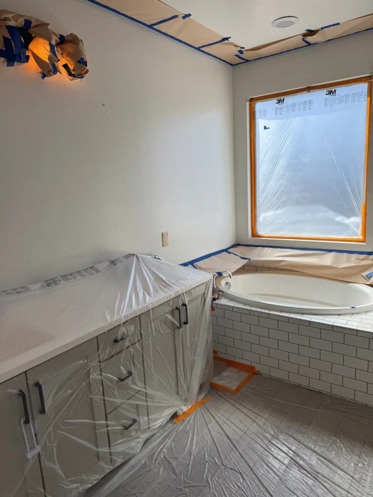 Bathroom with tub, vanity, window, and fixtures completely masked before interior painting
