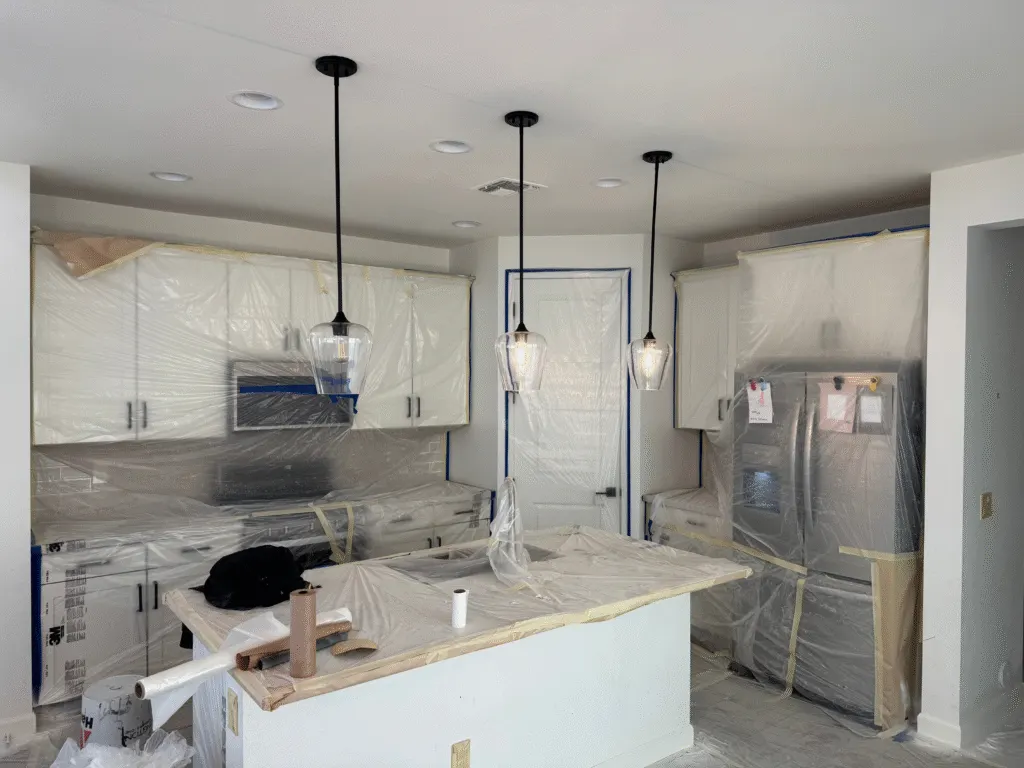 Kitchen with cabinets, appliances, and counters fully masked in plastic before painting
